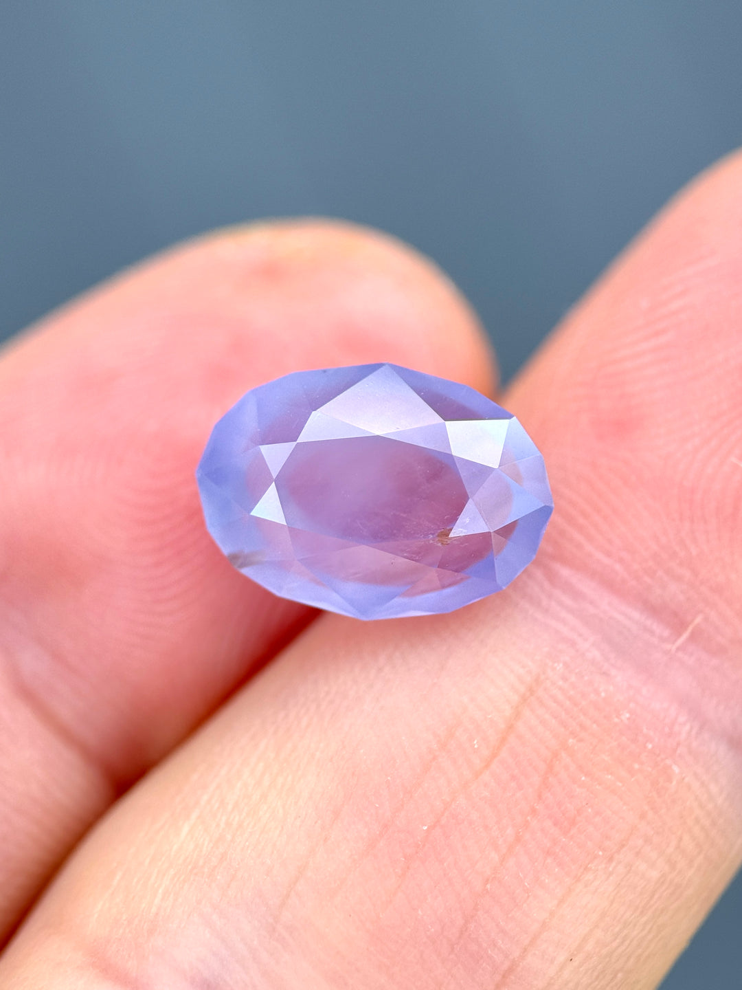 Oval violet sapphire on fingertip showing size scale and muted pastel color.
