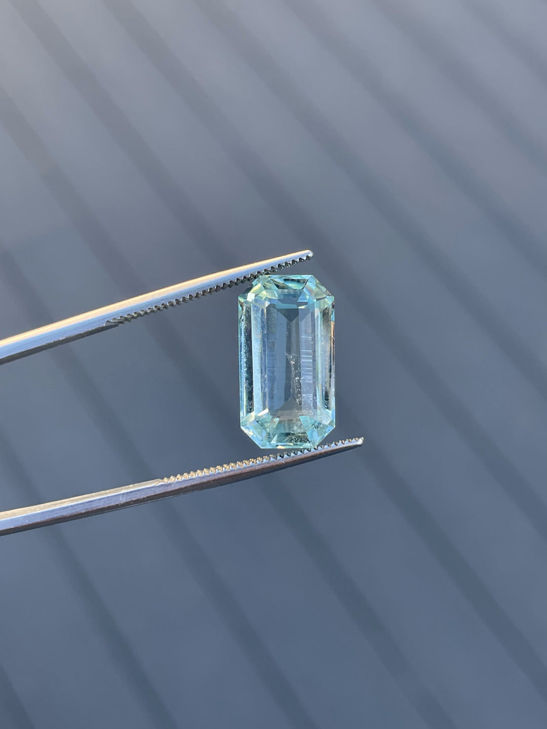 8.80-carat aquamarine gemstone with mint blue-green hues, captured in tweezers with a striking shadowed background.