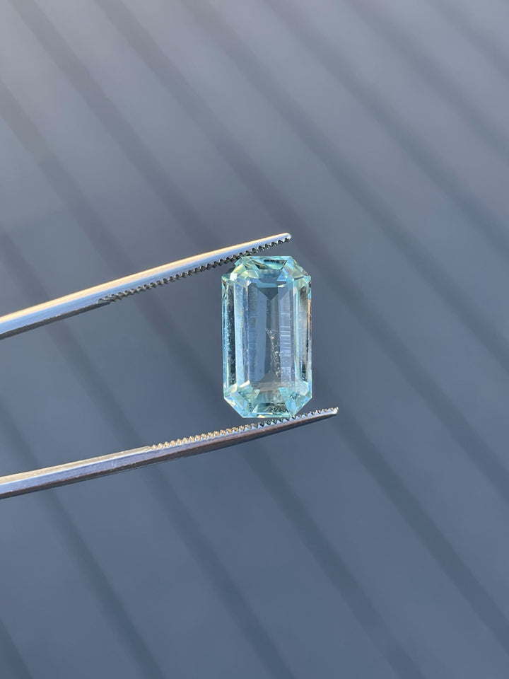 8.80-carat aquamarine gemstone with mint blue-green hues, captured in tweezers with a striking shadowed background.