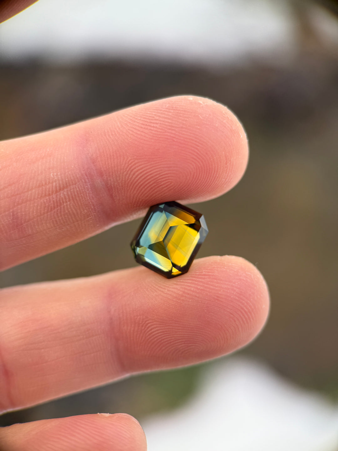 Angled view of a 9.14ct Nigerian parti sapphire emerald cut, showcasing strong yellow, green, and blue color separation and high clarity, Gombe origin