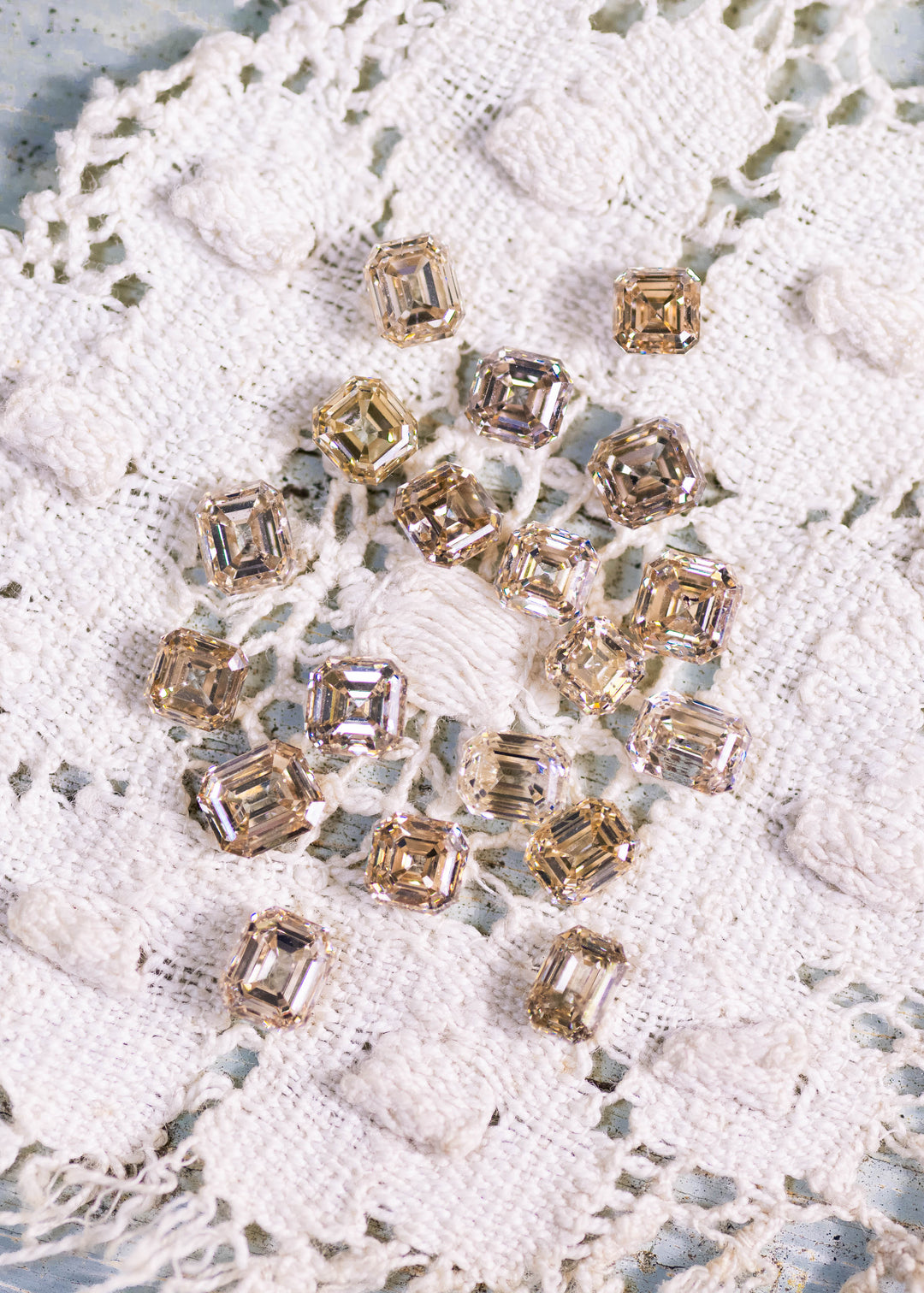 Matching set of champagne colored Asscher and emerald cut diamonds arranged on lace background showing step cut brilliance and uniform layout.