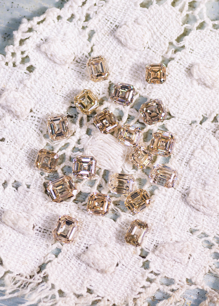 Matching set of champagne colored Asscher and emerald cut diamonds arranged on lace background showing step cut brilliance and uniform layout.