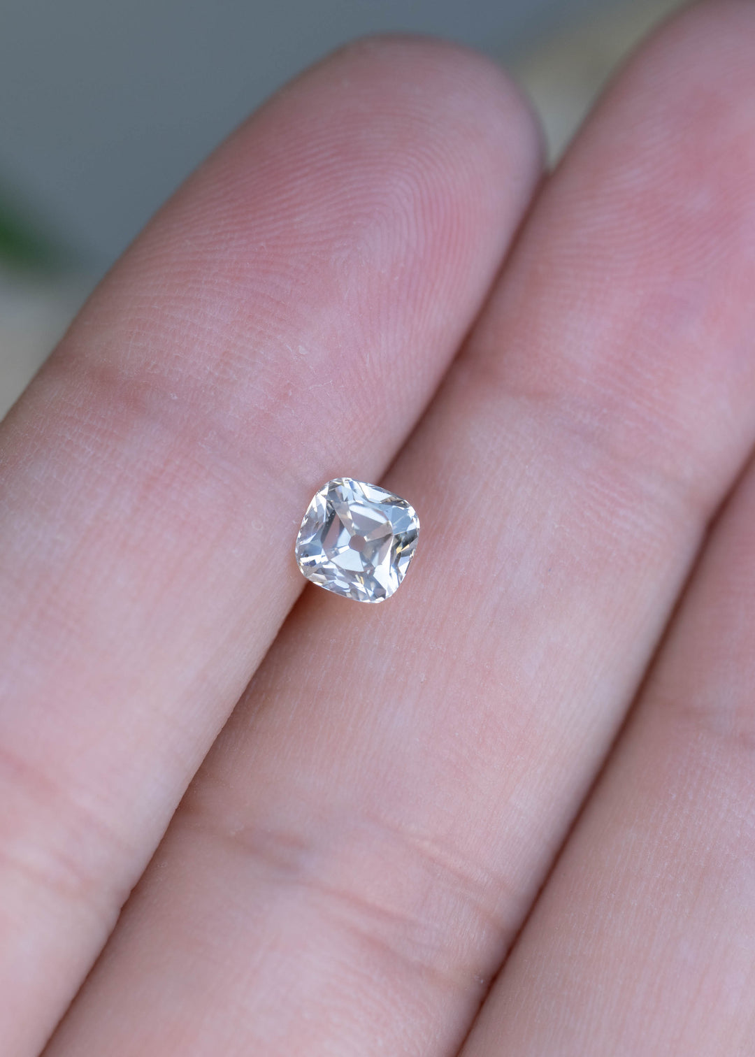 A 0.79 carat white antique cushion cut diamond resting on fingertips for scale, showcasing its softly rounded square outline and crisp precision faceting.
