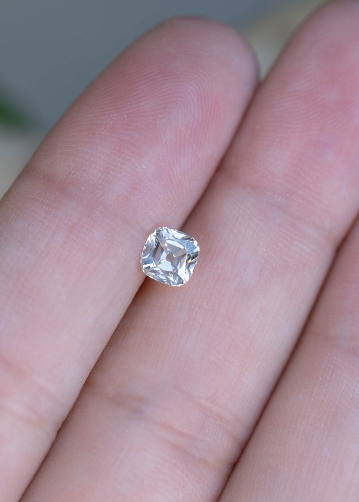 A 0.79 carat white antique cushion cut diamond resting on fingertips for scale, showcasing its softly rounded square outline and crisp precision faceting.