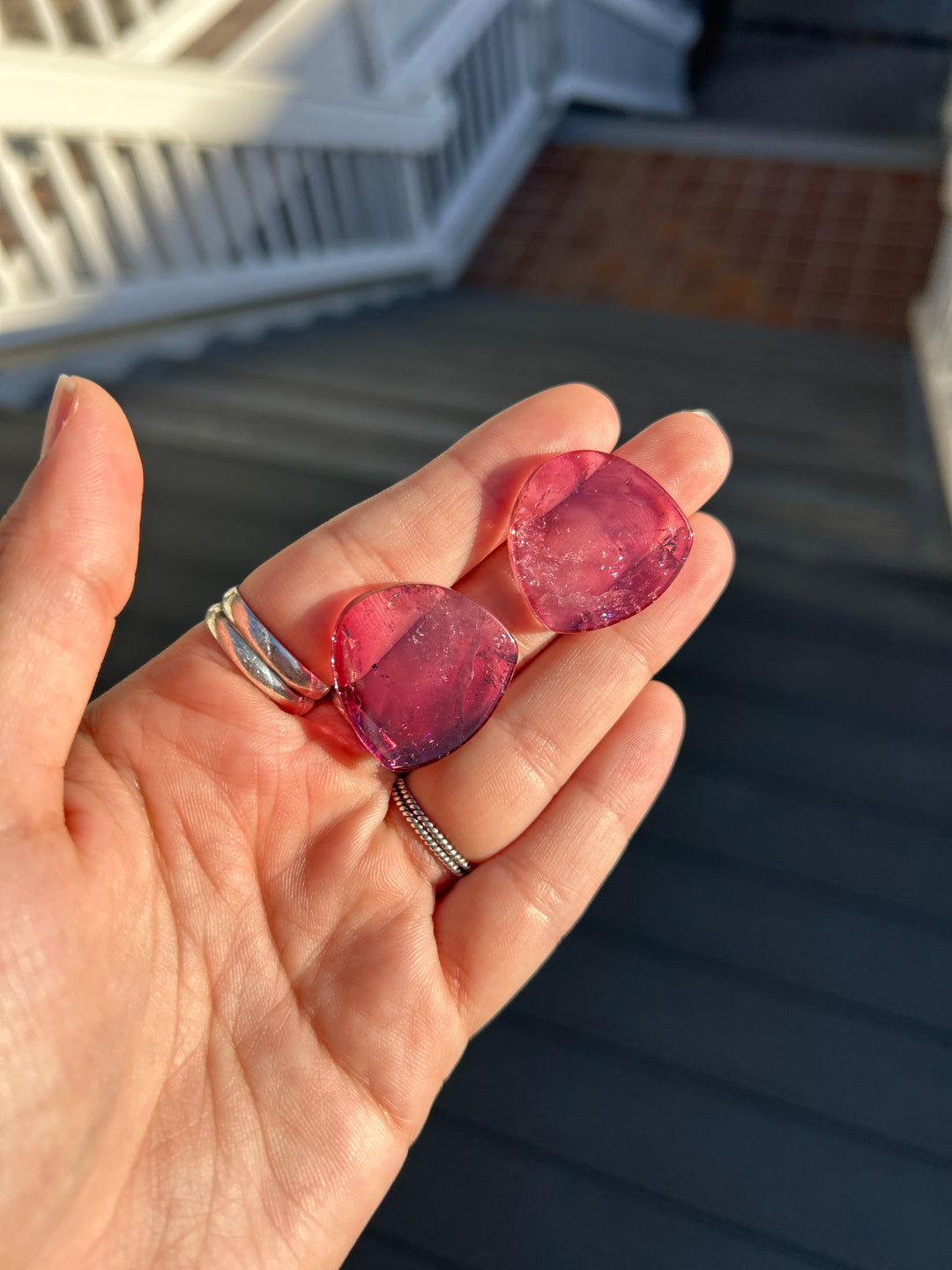 A matched pair of vibrant deep pink tourmaline slices from Congo, totaling 65.78 carats, photographed in direct sunlight. Their polished surfaces reveal rich raspberry-pink coloration, translucent crystal, and intricate natural internal features. Untreated and well suited for bespoke jewelry design.