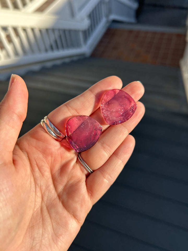 A matched pair of vibrant deep pink tourmaline slices from Congo, totaling 65.78 carats, photographed in direct sunlight. Their polished surfaces reveal rich raspberry-pink coloration, translucent crystal, and intricate natural internal features. Untreated and well suited for bespoke jewelry design.