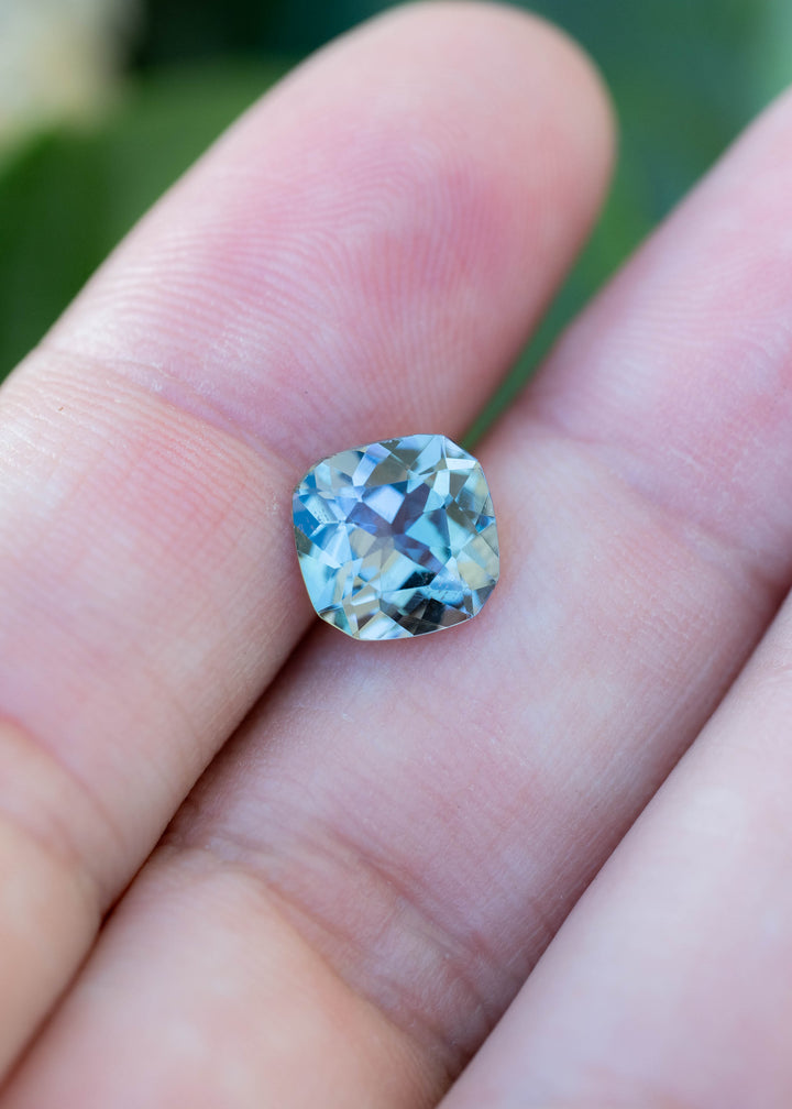 A rare 2.08 carat untreated Tanzanite resting on fingertips for scale, revealing its balanced square shape and striking teal, green, and purple color transitions.