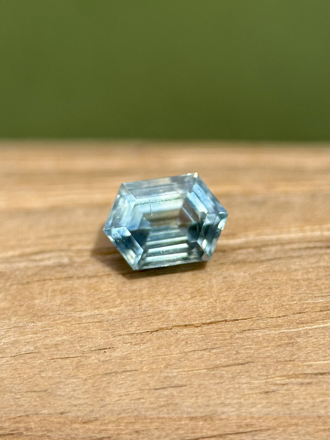 Close-up of 0.83 carat Montana sapphire with step cut hexagon shape and parti tones of teal, blue, and yellow on wood background