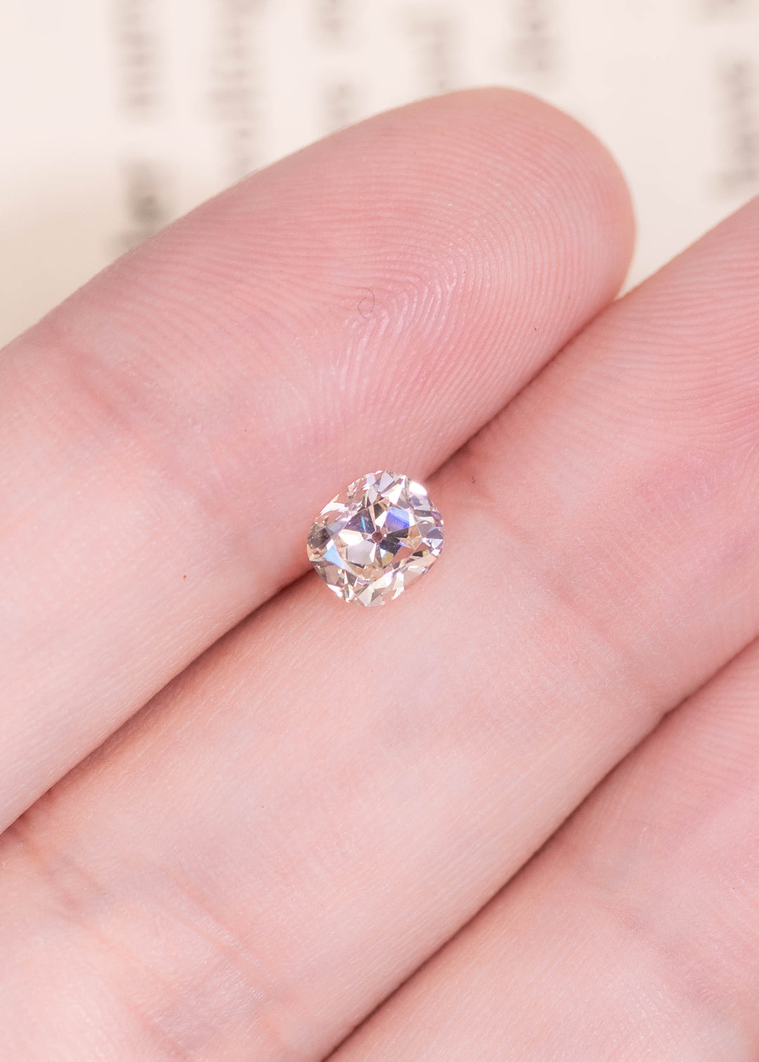 0.72ct old mine cut cushion diamond on fingertip showing size scale and vintage faceting pattern.