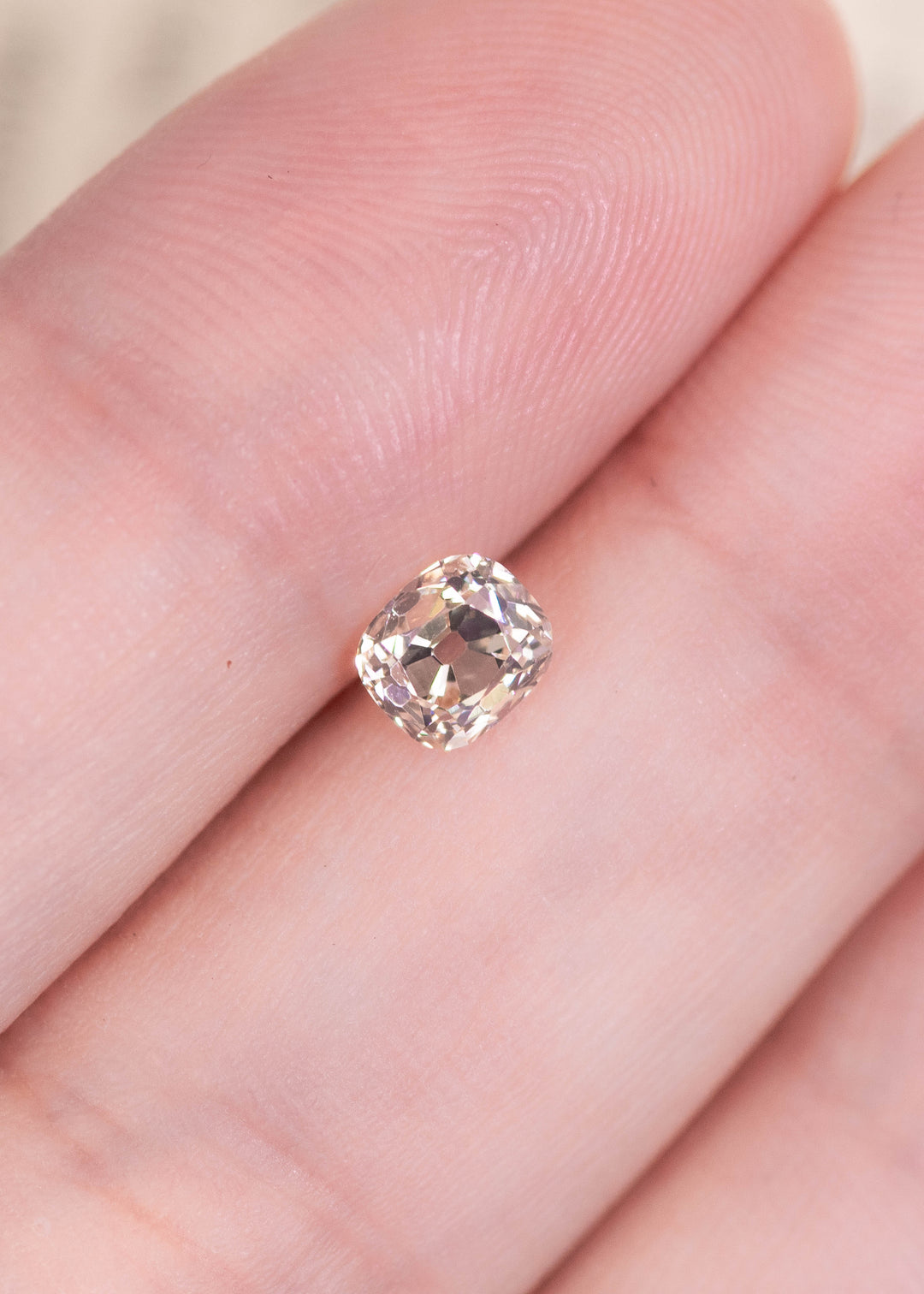 0.69ct old mine cut diamond on fingertip showing size scale and soft natural color.