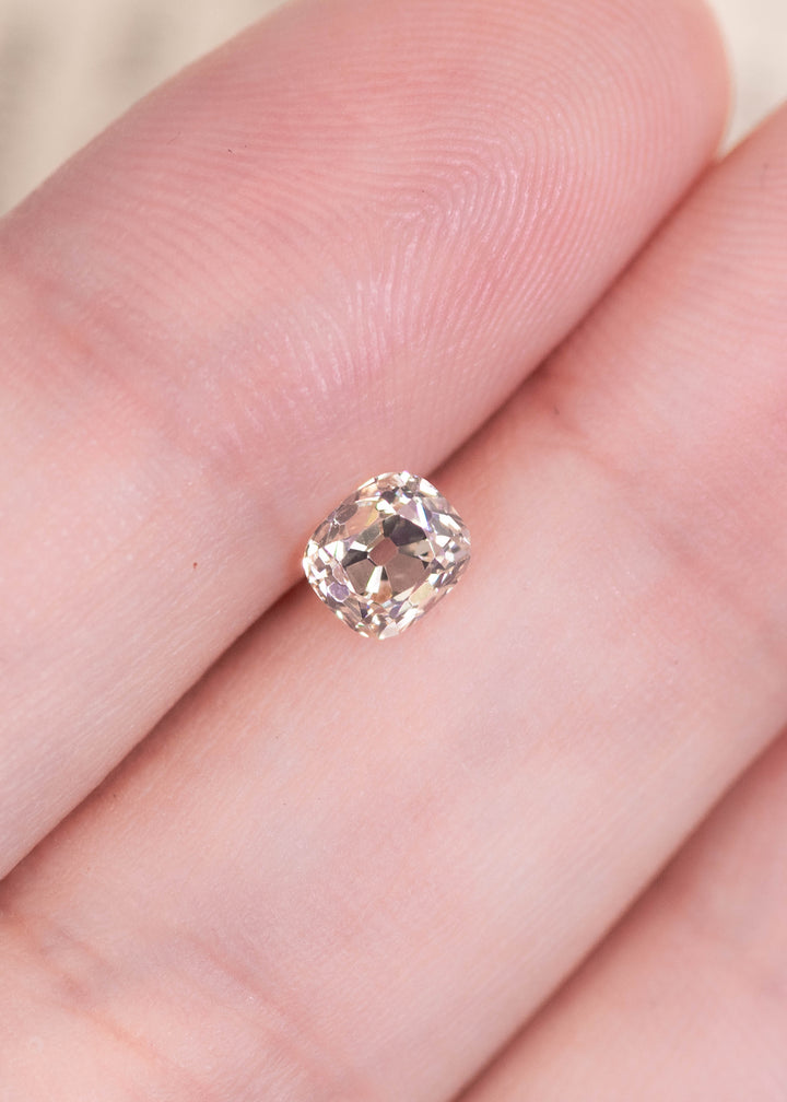 0.69ct old mine cut diamond on fingertip showing size scale and soft natural color.