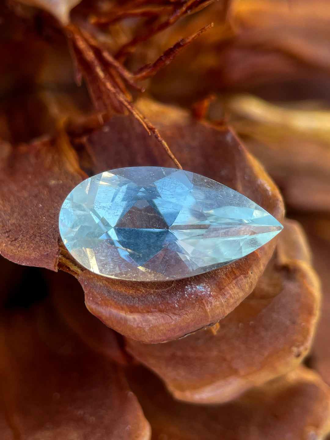 A radiant 3.88-carat aquamarine gemstone placed on a rustic pinecone, highlighting its green mint blue color and pear shape.
