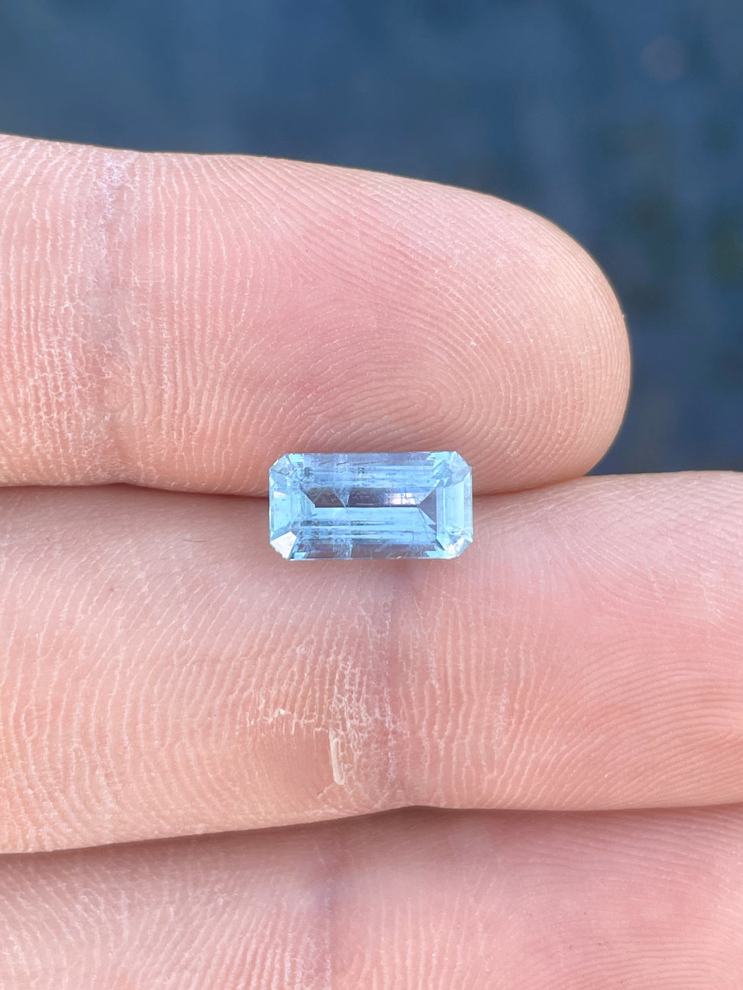 A beautiful emerald-cut aquamarine gemstone with a mint blue hue resting on a person's fingertip, showcasing its clear facets and vibrant color.
