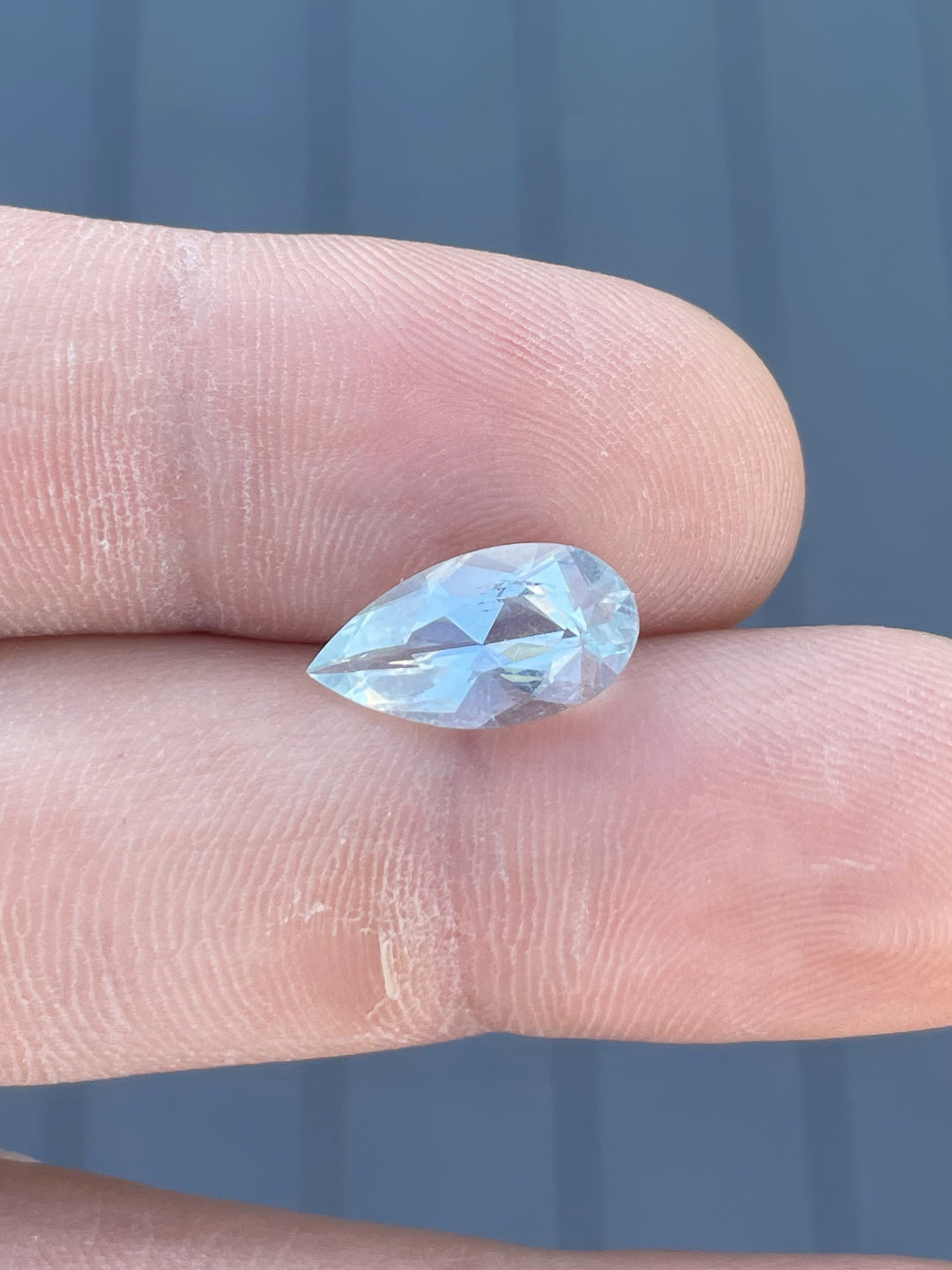 Close-up of a 3.88-carat aquamarine gemstone with a green mint blue hue, held on a fingertip under natural daylight.
