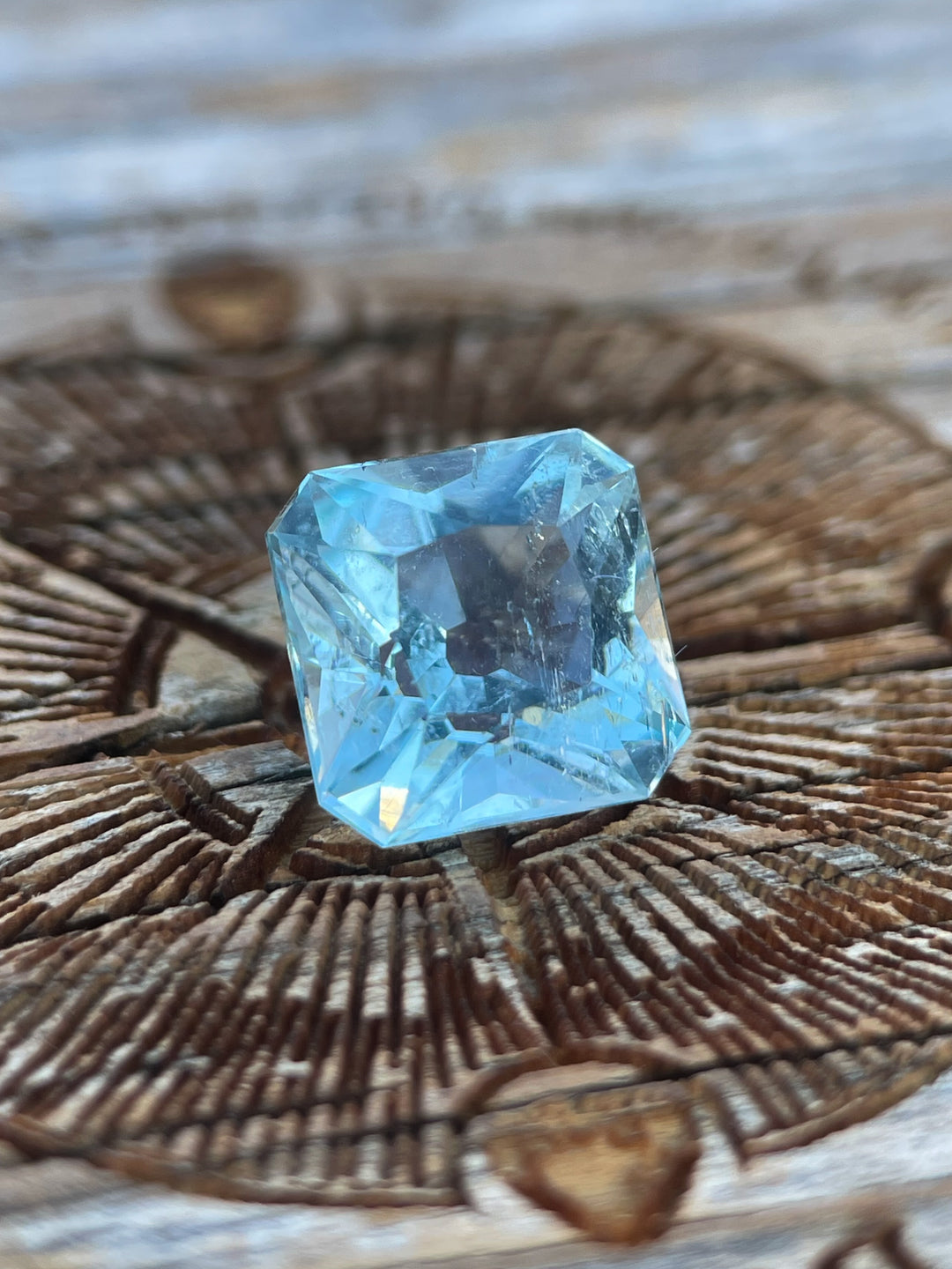 A close-up of a 2.87-carat aquamarine gemstone with a custom antique cushion cut, showcasing its intricate facets on a rustic wooden background.