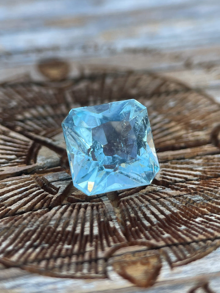 A close-up of a 2.87-carat aquamarine gemstone with a custom antique cushion cut, showcasing its intricate facets on a rustic wooden background.
