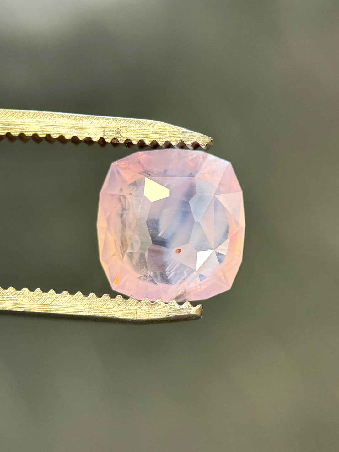 Pink opalescent sapphire from Sri Lanka held between tweezers against a dark background