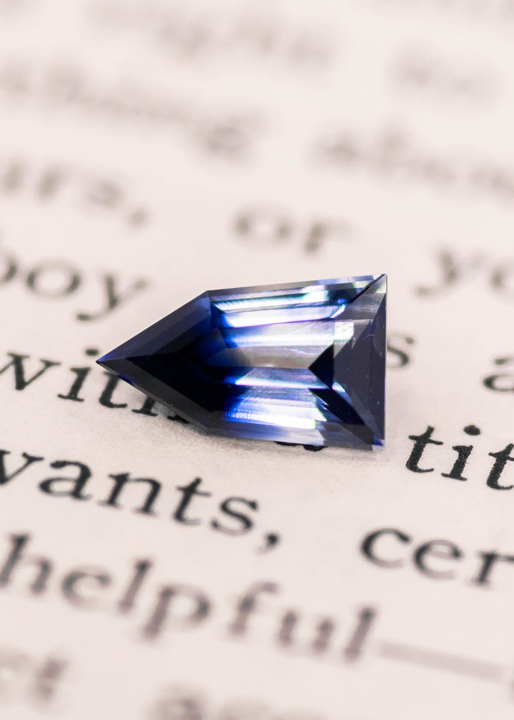Macro view of a bi-color parti sapphire on hand, displaying colorless and deep blue hues with geometric pentagon shield step cut, natural 1.22 carat sapphire from Ratnapura