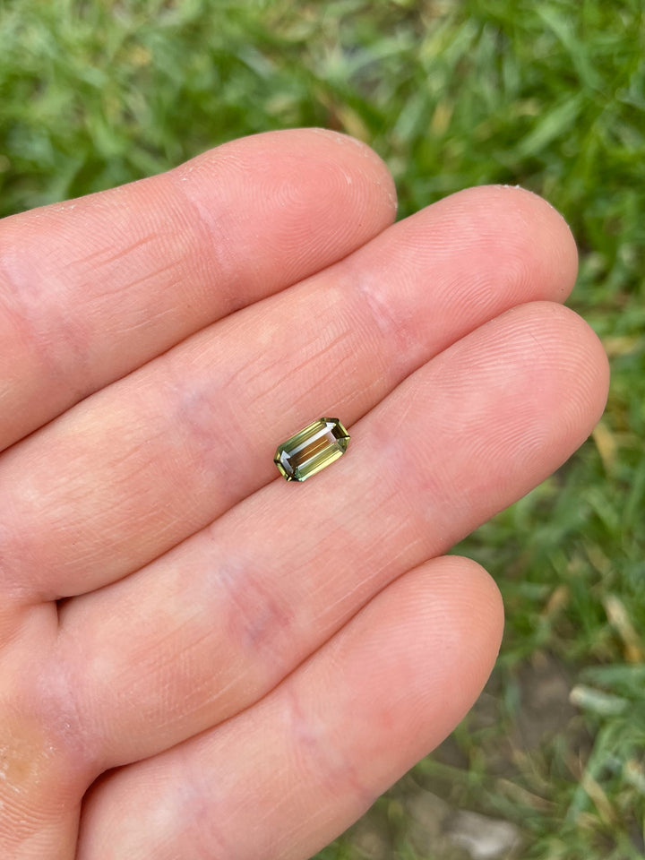 1.09 carat bi-color yellowish green to yellow sapphire photographed on hand to showcase natural octagonal step cut and size scale