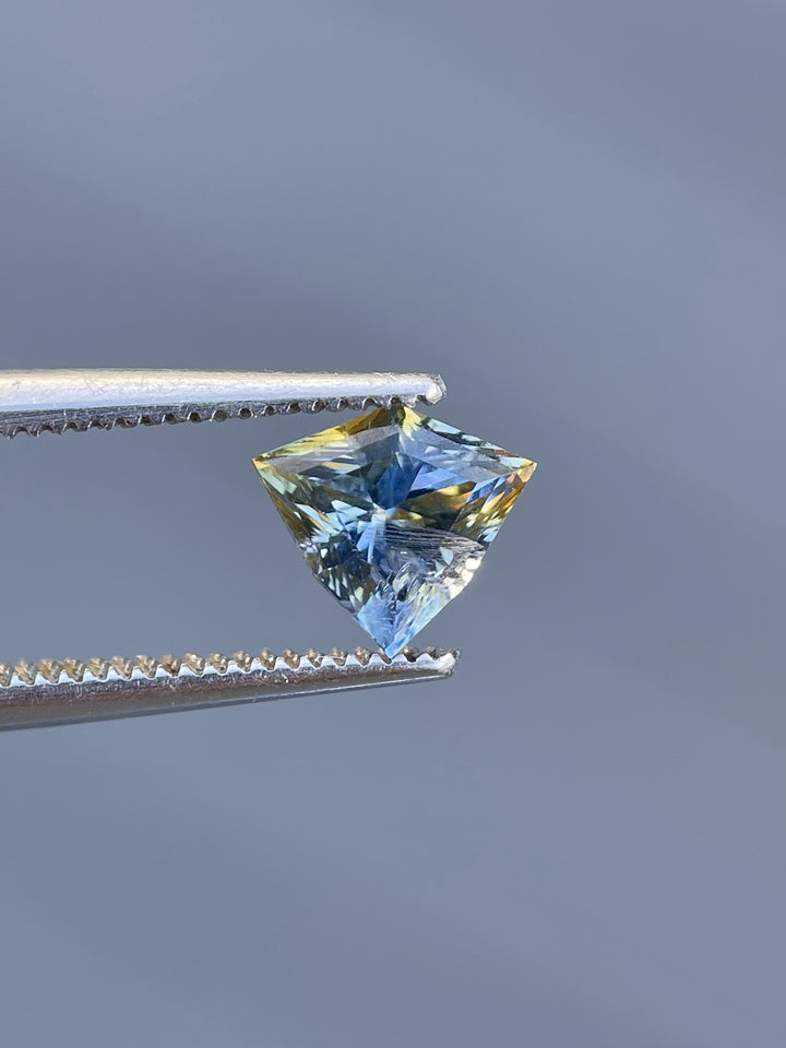 Stunning 1.58-carat bi-color yellow and cornflower blue sapphire in a mix step cut shield shape, sourced from Sri Lanka, displayed on a natural rock surface.
