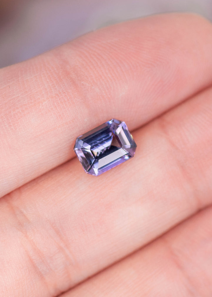 Loose 1.76ct modified emerald cut Tanzanite resting on fingers displaying vivid blue and purple color shift from Merelani Hills