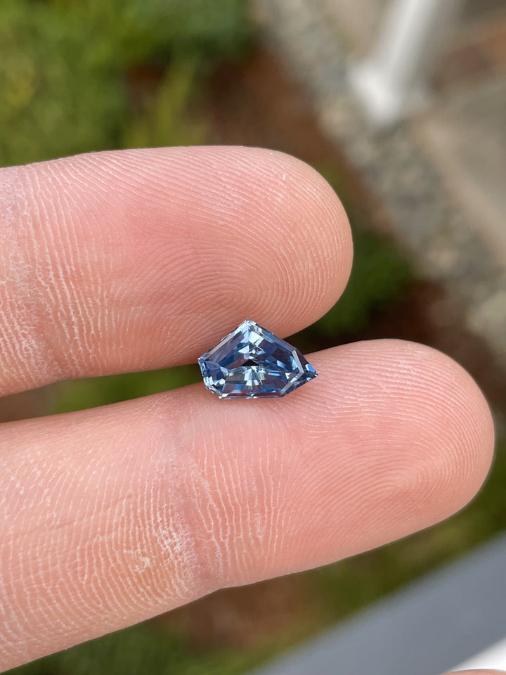 A 2.23-carat blue sapphire, free-form geometric cut, delicately held between fingers, highlighting its captivating brilliance and natural blue hue. Origin: Sri Lanka, Untreated.