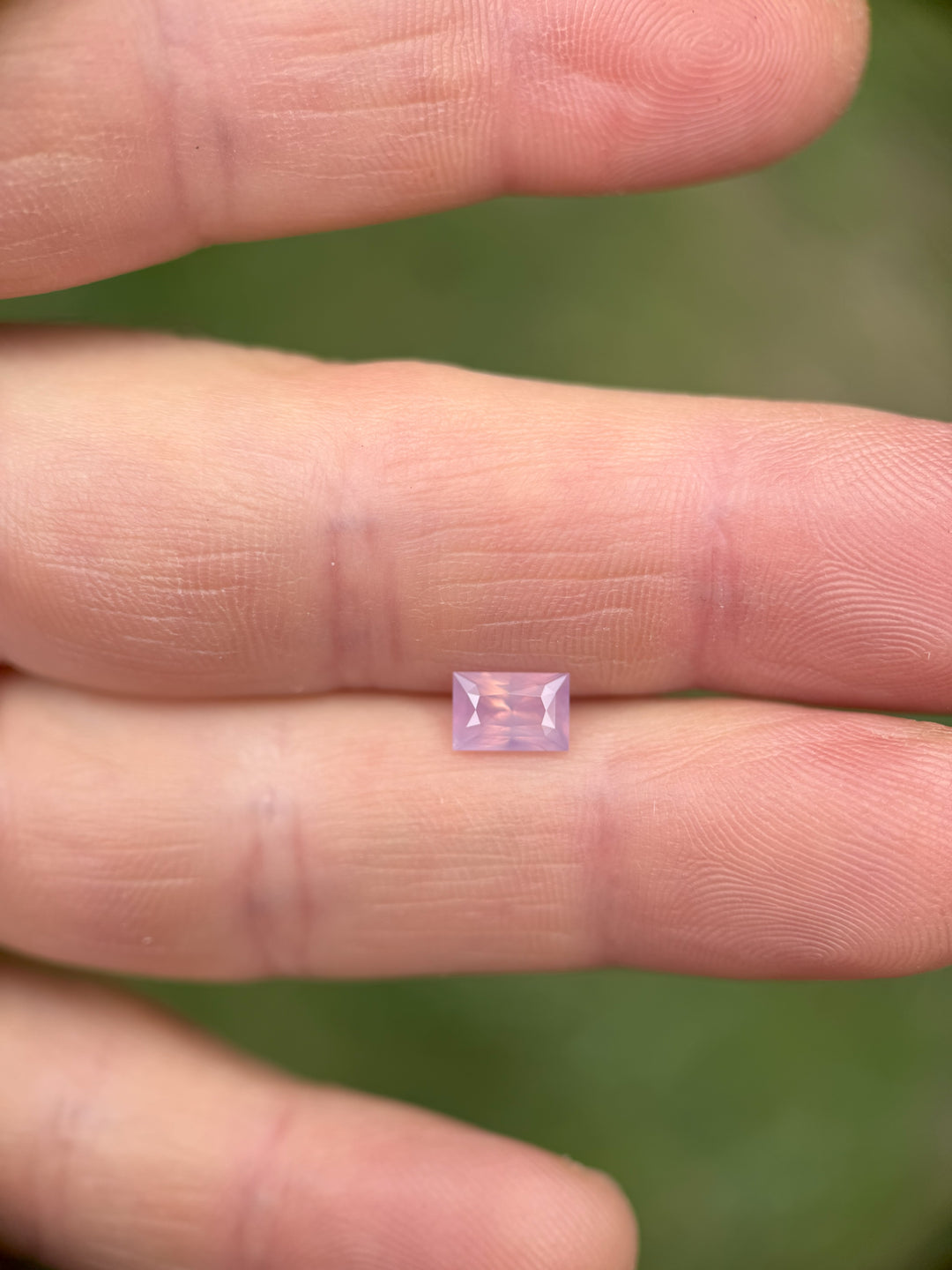 1.20-carat blush pink opalescent sapphire in a precision baguette mixed cut, displayed on fingertips for scale.