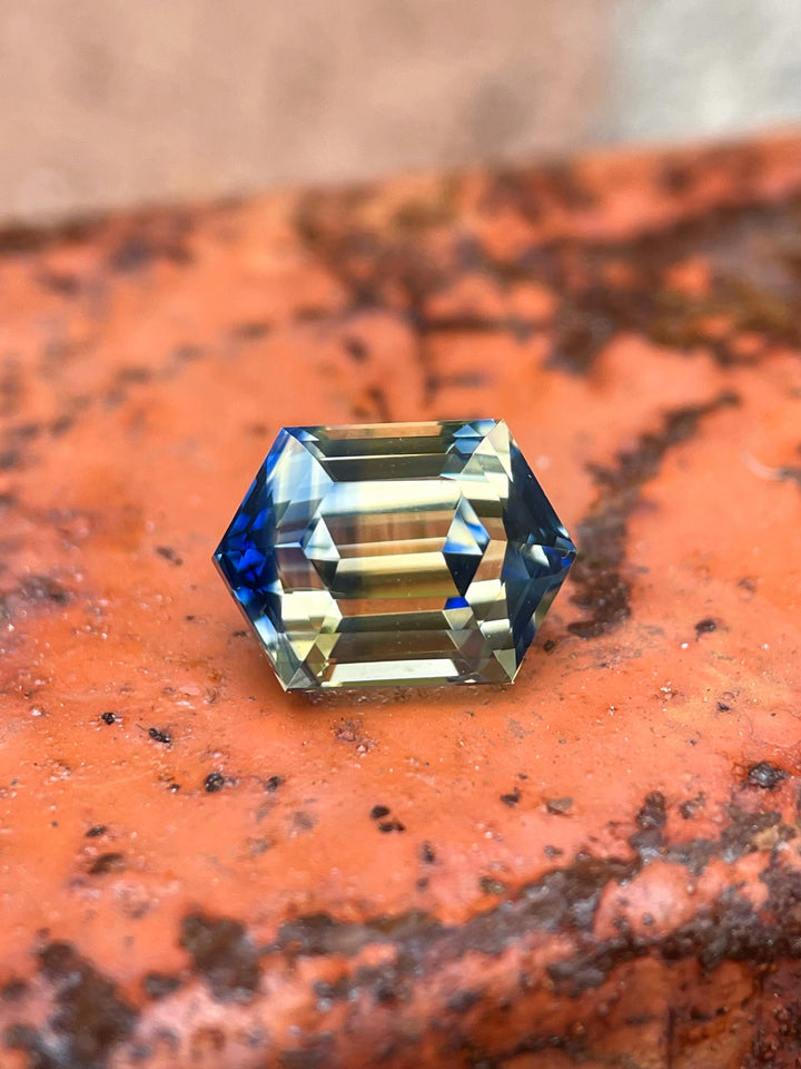 Sapphire displayed on textured brick, showcasing vivid unheated yellow and blue tones with a symmetrical hex step cut.