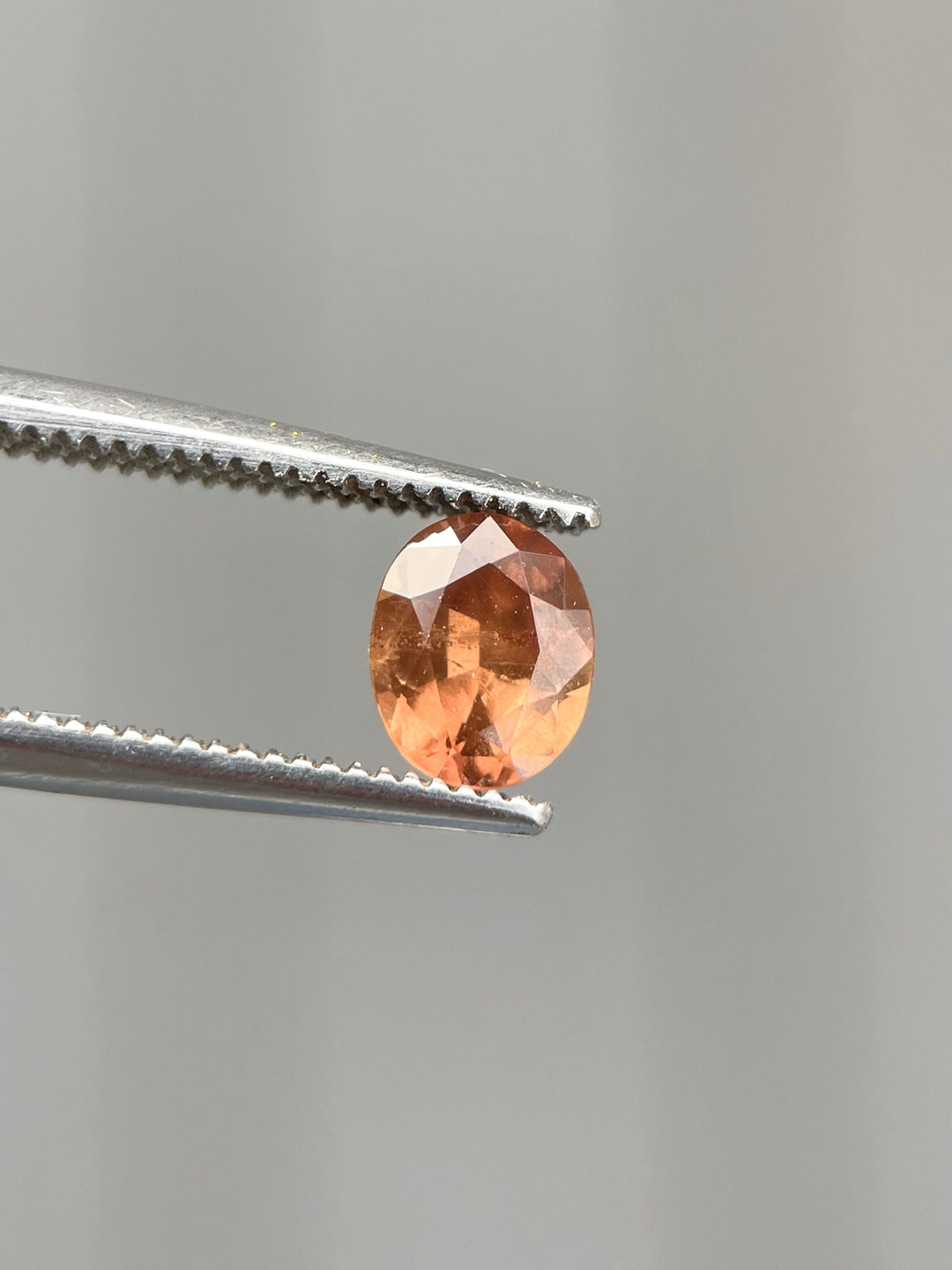 A 0.95-carat brown-orange sapphire with a modified brilliant oval cut, set against a textured yellow lichen background. The stone has vibrant hues of orange and brown with a smooth, polished surface.