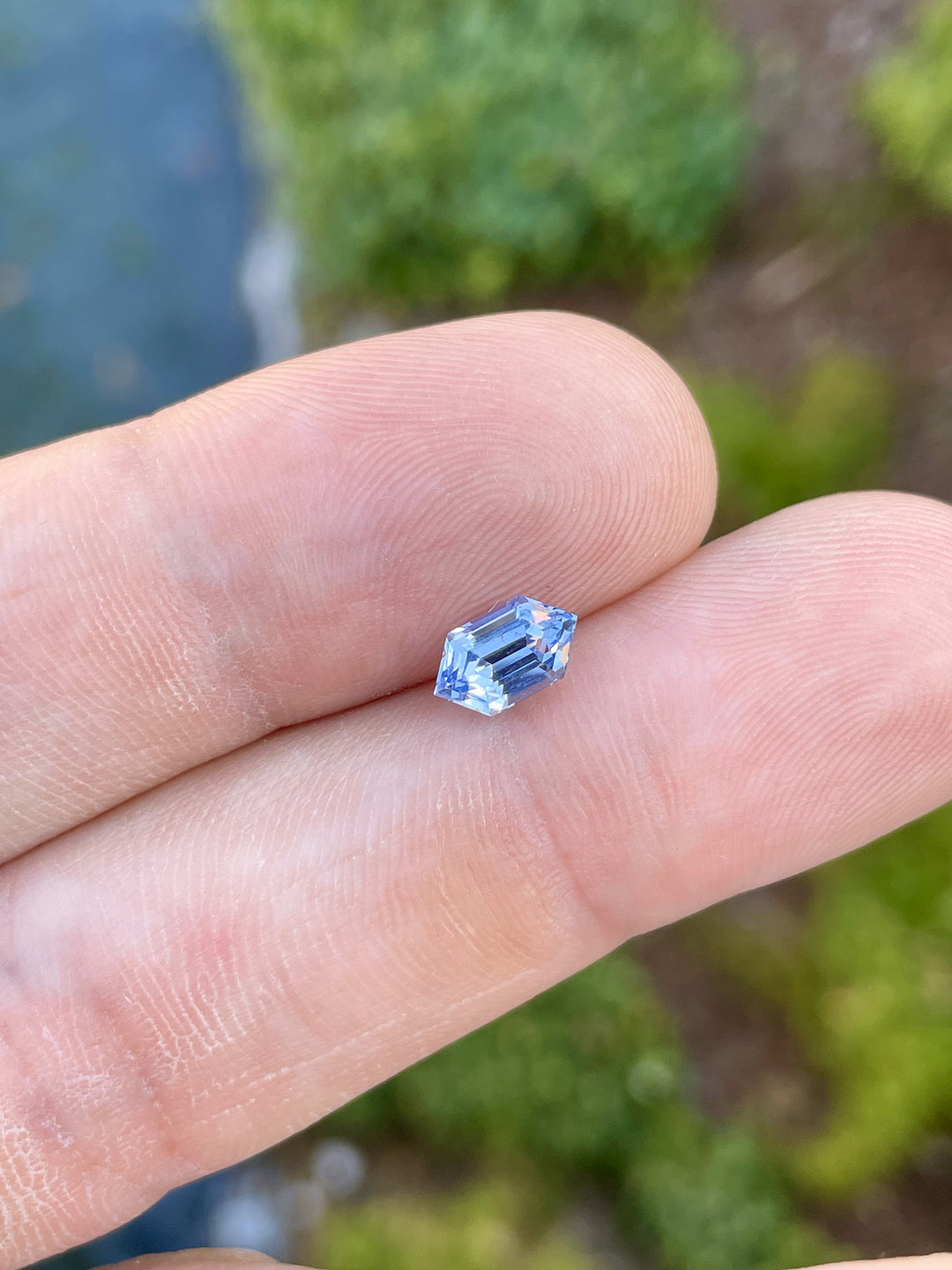 A 1.62-carat light Ceylon blue sapphire, displayed on a fingertip for scale, highlights the stone's step-cut hexagonal shape and vivid blue hues. The gem's precision cut and dimensions, 8.78mm by 5.06mm by 4.50mm, reflect its quality and untreated nature. Sourced from Sri Lanka.