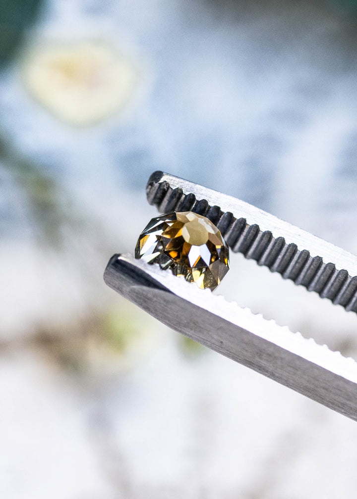Loose fancy yellow brown Mughal cut diamond angled in tweezers, revealing intricate historic faceting and warm golden reflections.