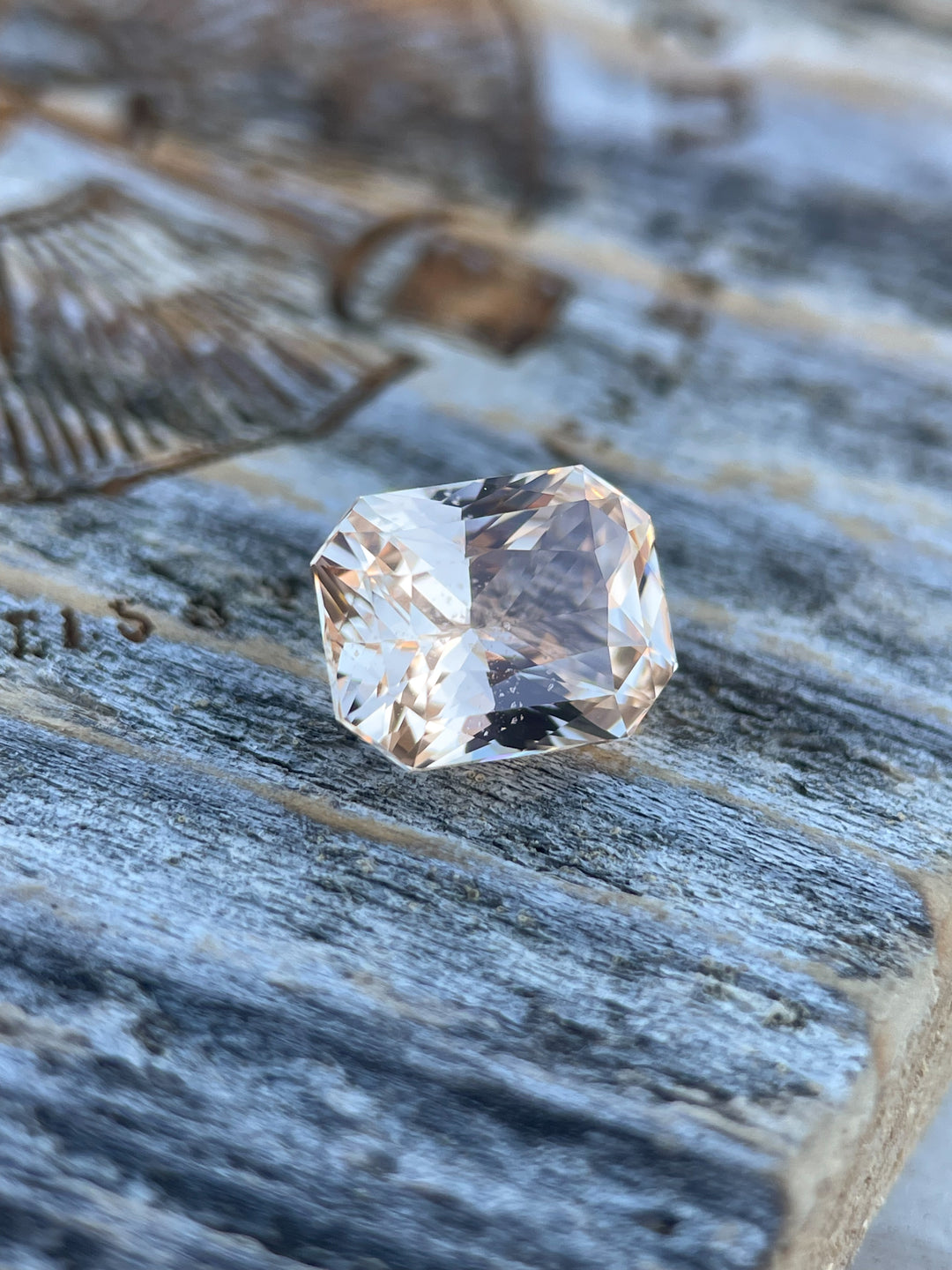 A beautifully faceted 2.55-carat sapphire with peach and champagne hues, displayed on a rustic textured background. Ethically sourced from Sri Lanka, untreated, and cut in an octagonal mixed style.