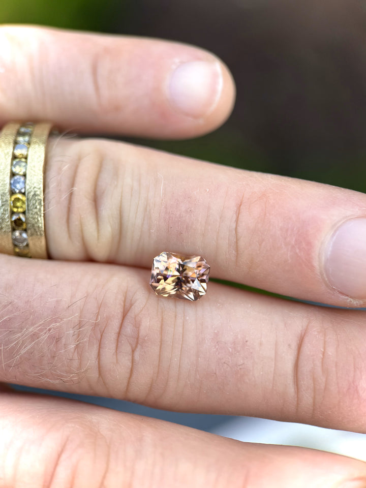 Macro shot of a 2.51 carat Tanzanite on skin, capturing brilliant internal reflections in orange, lavender, and peach with radiant faceting.