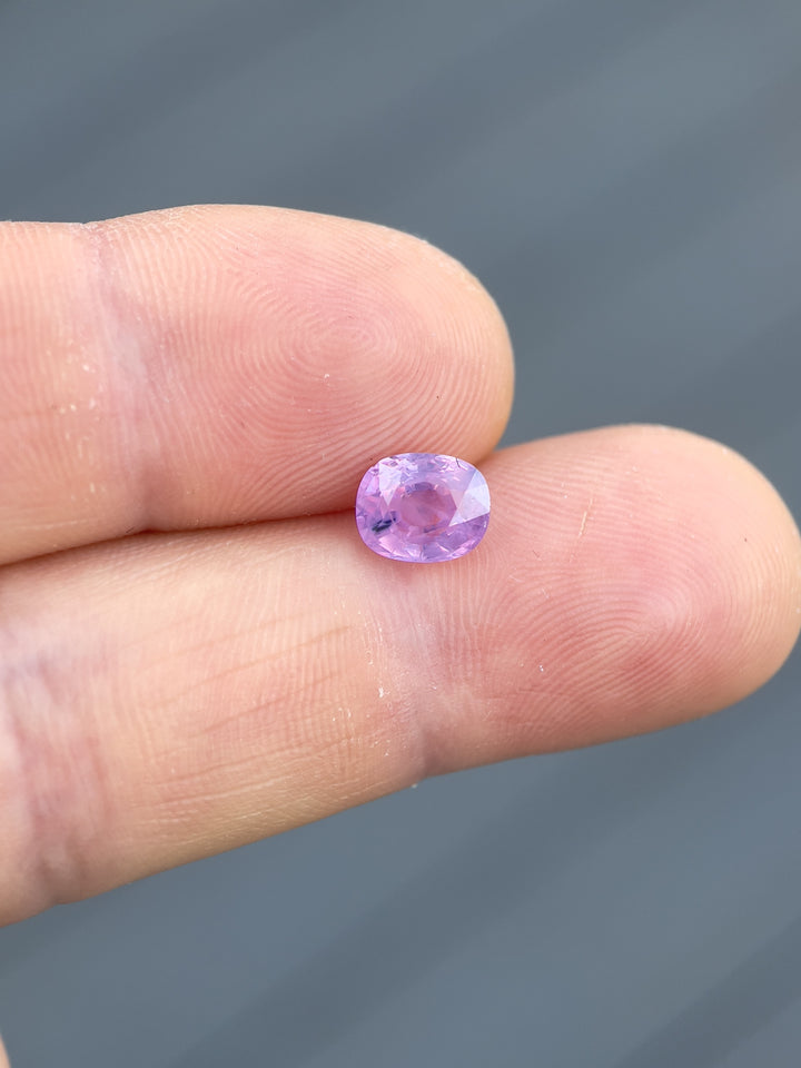 1.77ct opalescent pink and purple sapphire held between fingers, highlighting its mix cushion cut and vibrant colors, sourced from Luc Yen, Vietnam, with dimensions 7.53 x 6.13 x 4.42 mm.