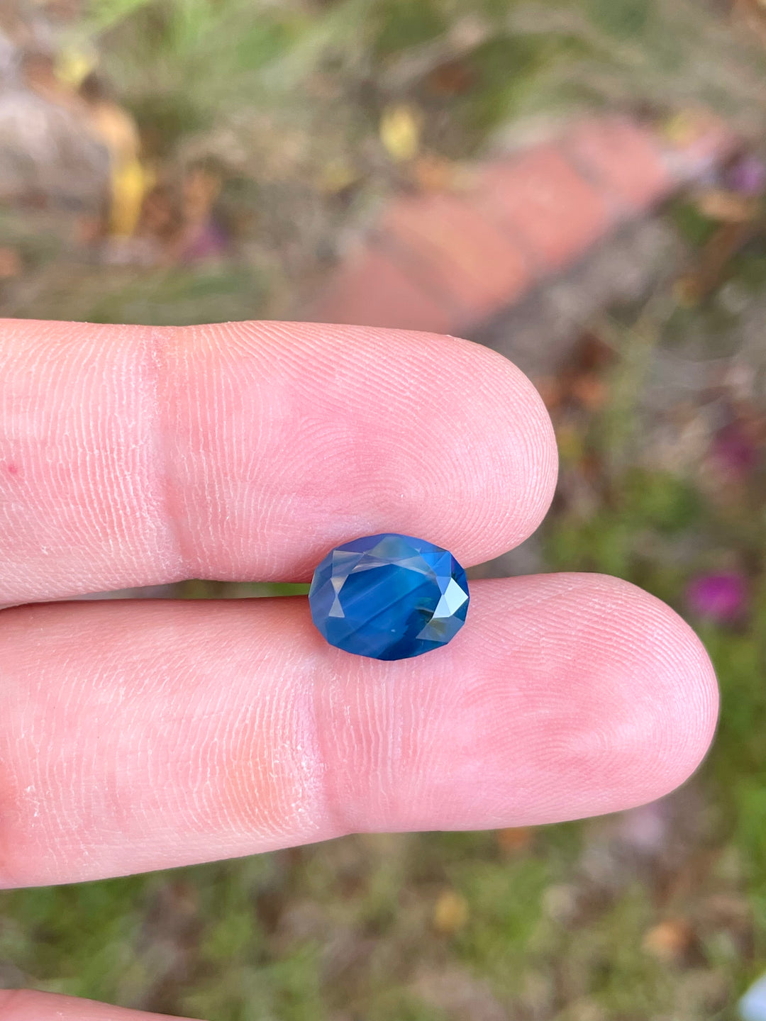 Close-up of a 5.23 carat oval sapphire, vivid colors of blueberry, green, and teal, originating from Gombe, Nigeria, with no treatment.