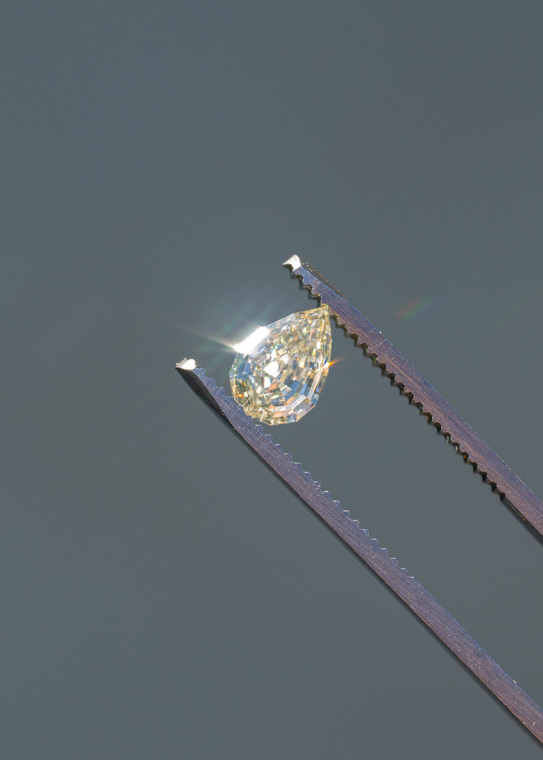 Close-up of a Light Yellow Geo Pear diamond sparkling in direct sunlight while held in tweezers, revealing bright flashes and architectural step faceting.