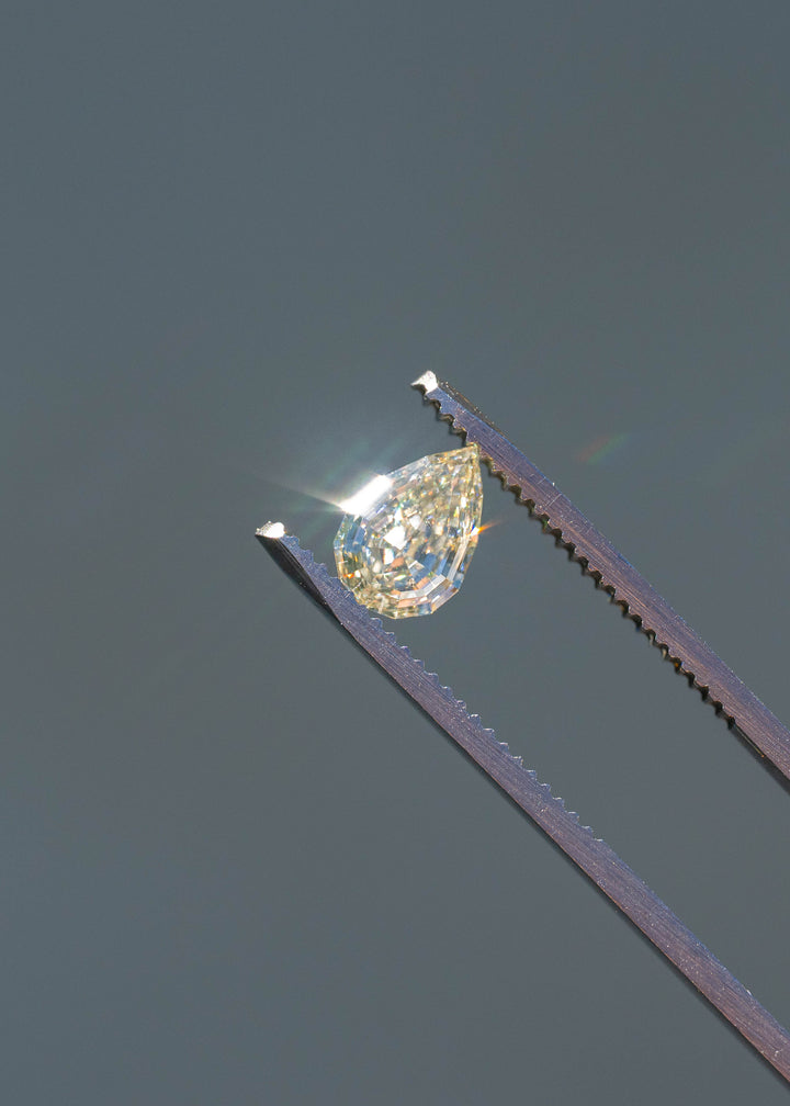 Close-up of a Light Yellow Geo Pear diamond sparkling in direct sunlight while held in tweezers, revealing bright flashes and architectural step faceting.