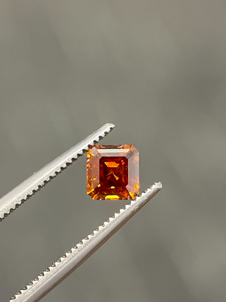 Close-up of a 1.01-carat cognac red diamond held in precision tweezers, highlighting its octagonal step cut and vibrant fiery tones.