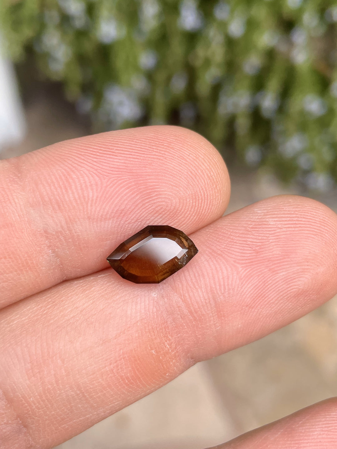 A 3.78-carat earthy brown cognac sapphire sits on a fingertip, highlighting its custom leaf portrait cut and smooth surface. The sapphire from the Umba River, Tanzania, is untreated and measures 12.76mm by 4.78mm by 3.80mm.