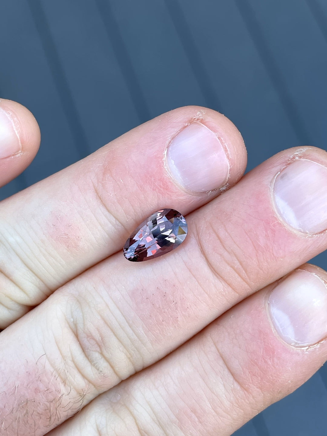  A stunning 3.09-carat color-change sapphire from Songea, Tanzania, displaying pink-to-brown hues in a pear brilliant cut, showcased on a fingertip.