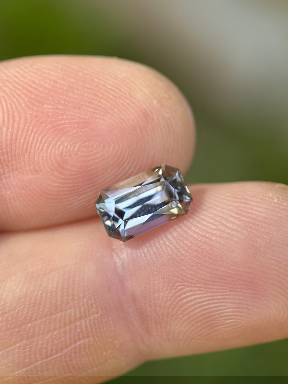 Natural unheated 2.32ct tanzanite gemstone in radiant cut on human fingertip with visible teal, blue, and green color shift