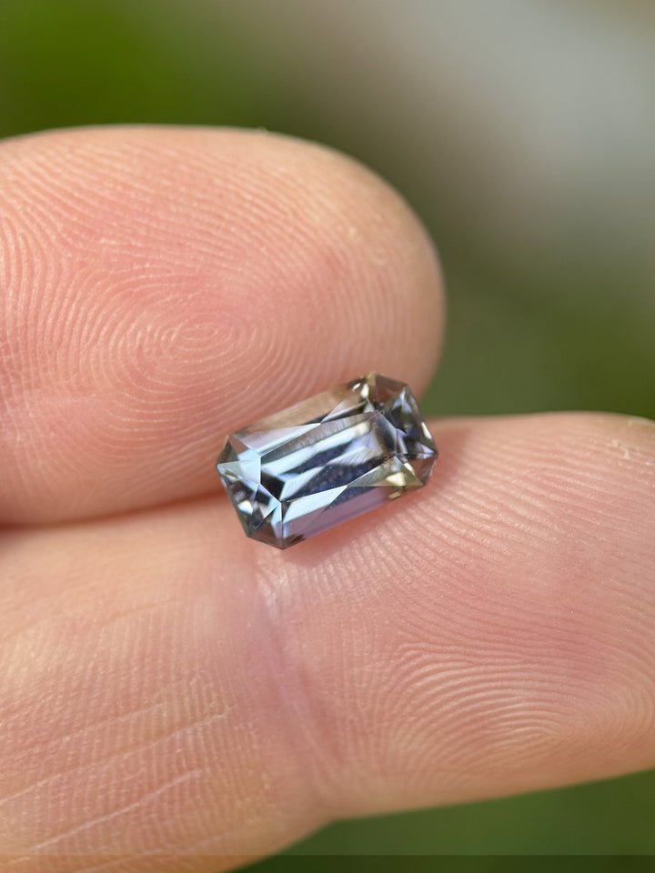 Natural unheated 2.32ct tanzanite gemstone in radiant cut on human fingertip with visible teal, blue, and green color shift