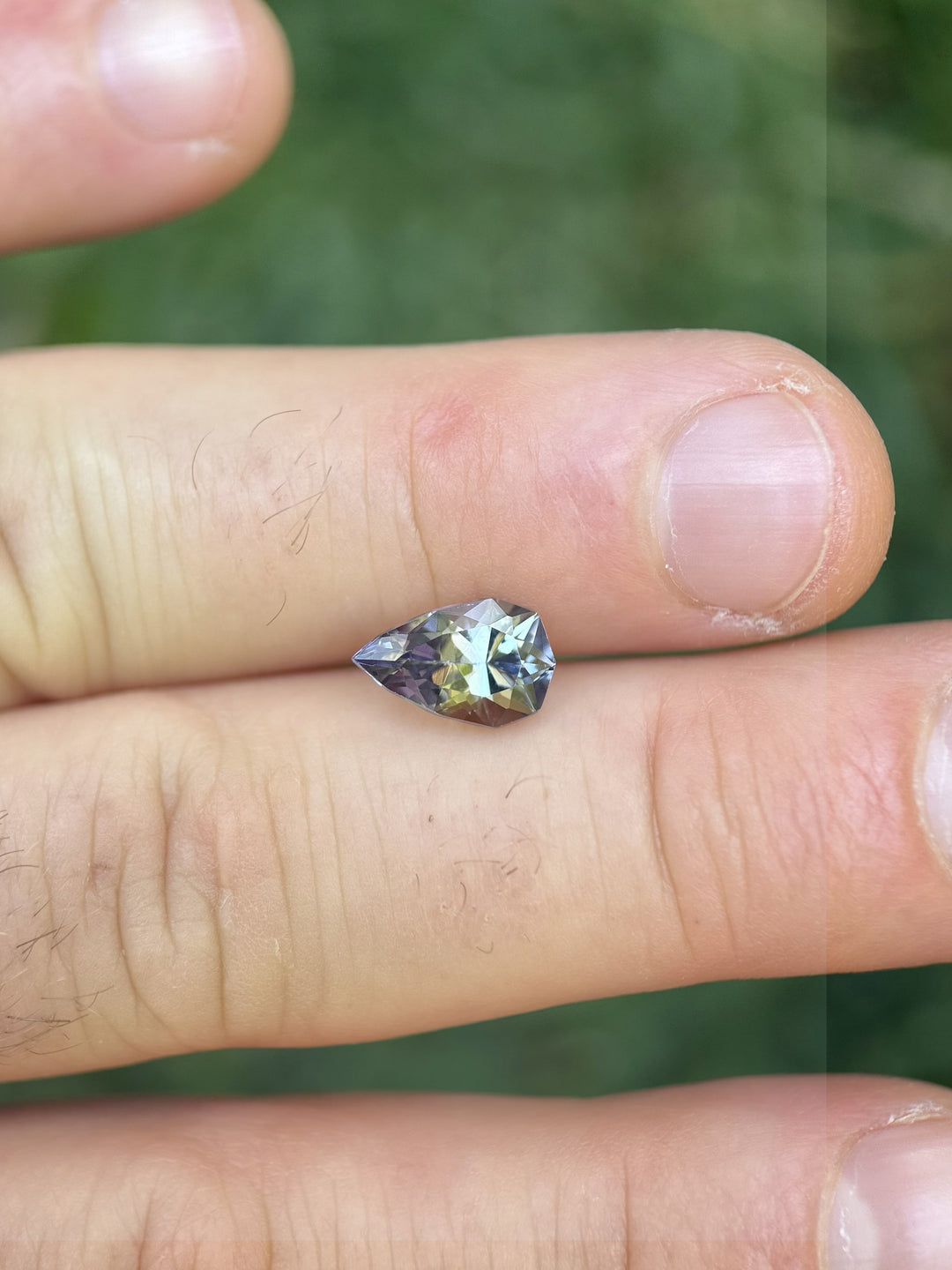 Colorful Tanzanite pear-shaped gem showing mermaid tones of green, yellow, and purple resting on fingers – 2.46 carats from Merelani Hills