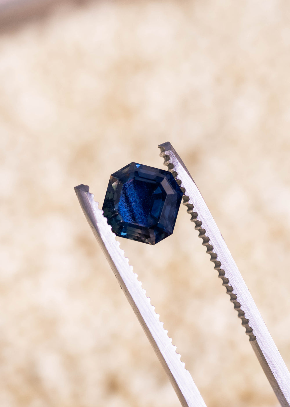 Loose teal blue to mauve sapphire held in tweezers, highlighting the precision Asscher cut and natural color shift from Nigeria.
