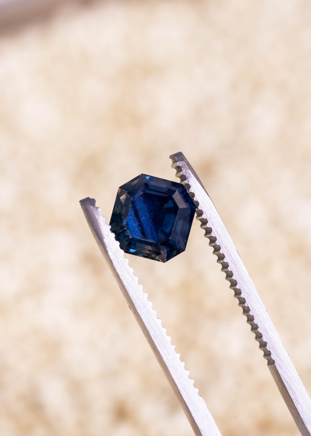 Loose teal blue to mauve sapphire held in tweezers, highlighting the precision Asscher cut and natural color shift from Nigeria.