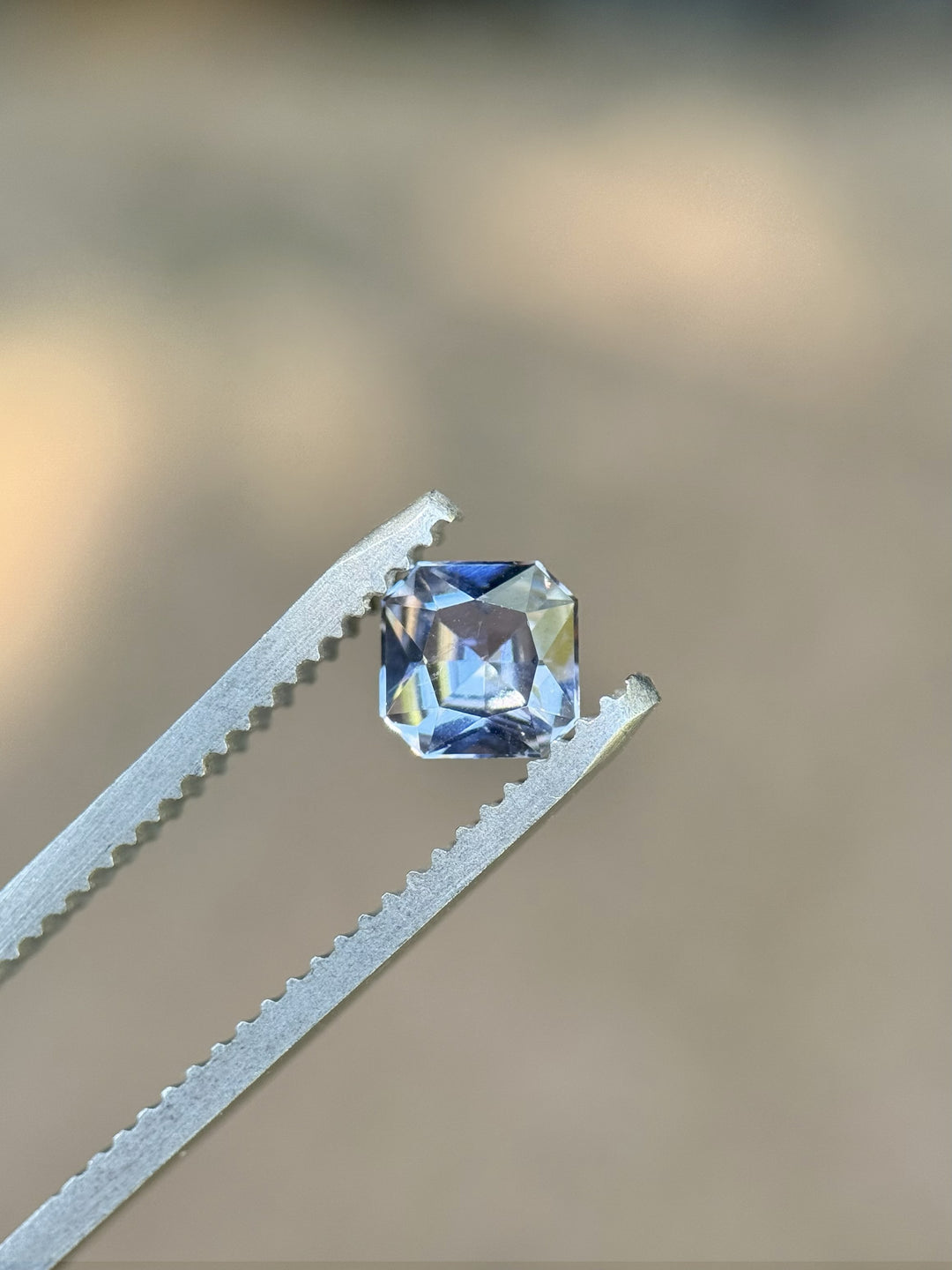 0.67ct color shift sapphire in custom squared radiant cut held in tweezers, showing sky blue and lilac hues – Umba River, Tanzania, no heat
