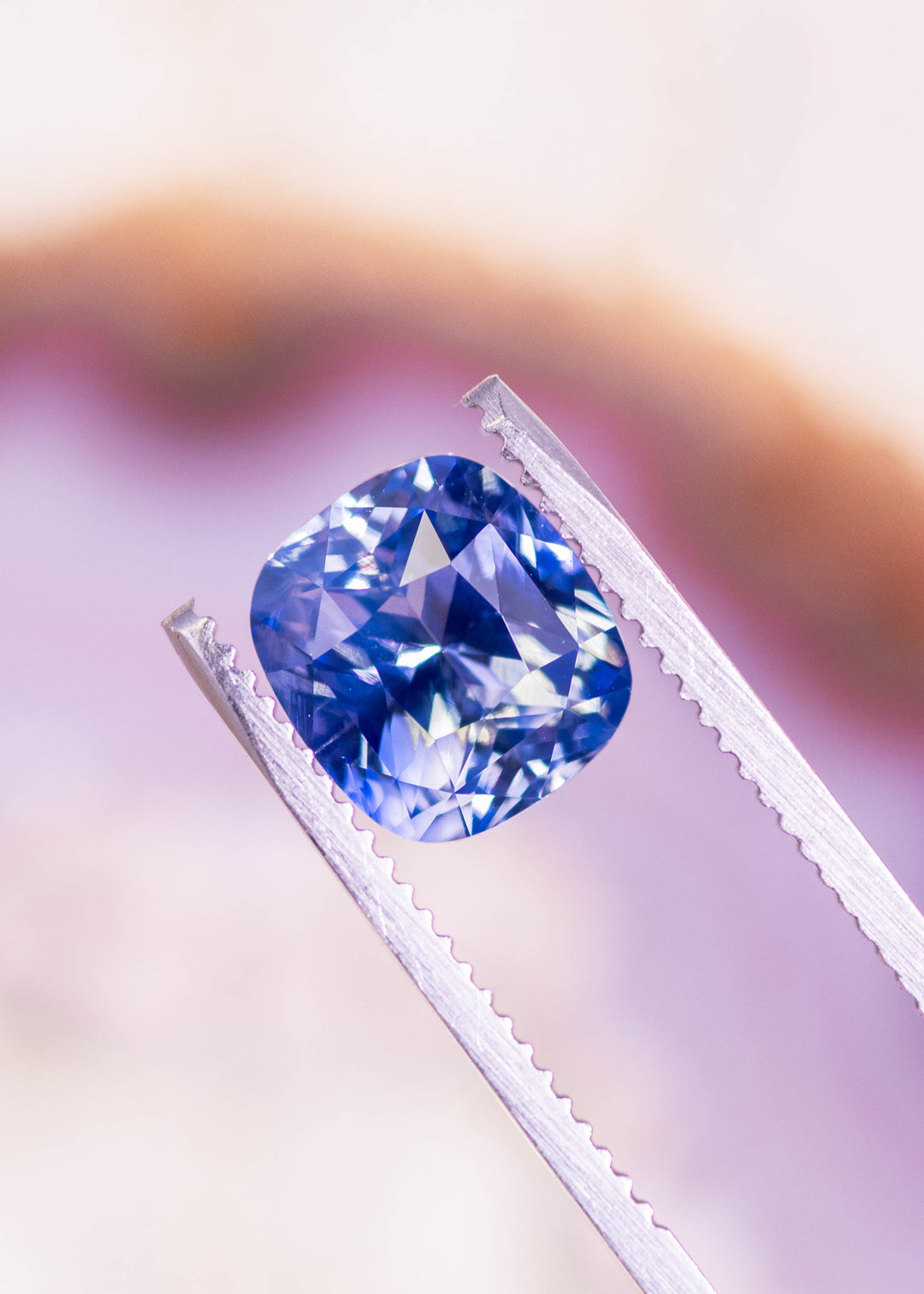 Loose gradient cornflower blue sapphire from Madagascar held in tweezers showing the brilliance and facet structure of the precision elongated cushion mixed cut.