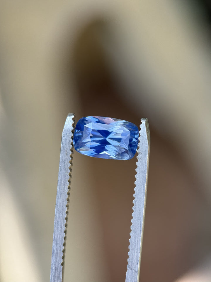 Close-up of 2.30CT cornflower blue sapphire held in gem tweezers, highlighting elongated cushion mixed cut and natural unheated color from Diego, Madagascar.