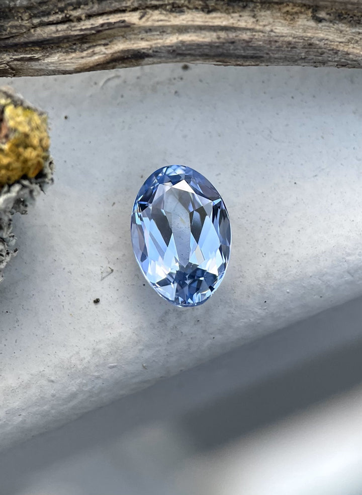 A mix-cut oval sapphire in cornflower blue, weighing 2.50 carats, elegantly placed on a wooden surface to emphasize its brilliance and untreated purity.