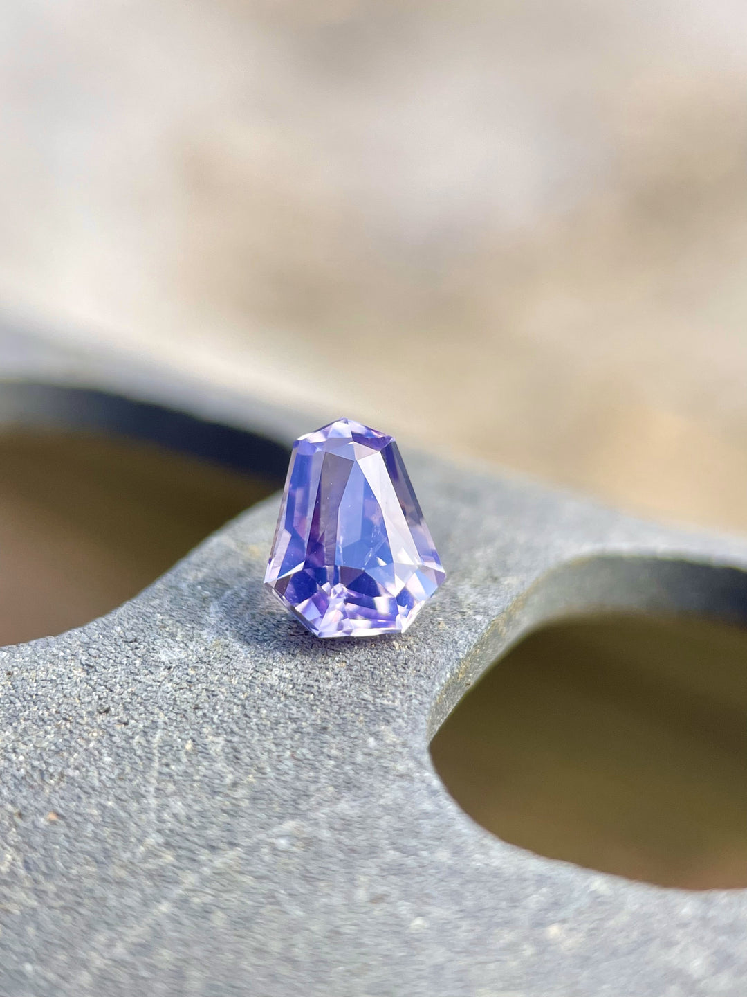 Artful display of a 1.14 carat sapphire with pink, lavender, and blue tones, positioned on a wooden surface, emphasizing its custom shield cut and flawless appearance.